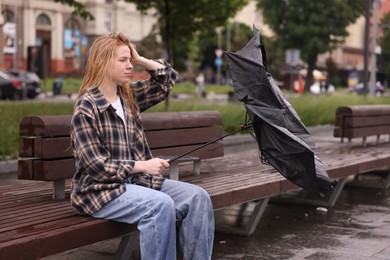 Photo of Frustrated woman with broken umbrella on bench outdoors