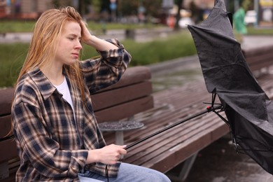 Photo of Frustrated woman with broken umbrella on bench outdoors