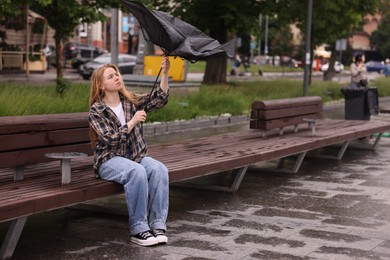 Photo of Woman with broken umbrella on bench outdoors