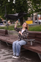 Photo of Woman with broken umbrella on bench outdoors