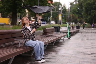 Photo of Woman with broken umbrella on bench in park