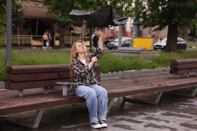 Photo of Woman with broken umbrella on bench outdoors