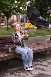 Photo of Woman with broken umbrella on bench outdoors