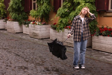 Photo of Frustrated woman with broken umbrella on city street. Space for text
