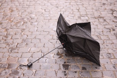 Photo of Broken black umbrella on wet pavement outdoors