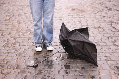 Photo of Woman and broken umbrella on wet pavement outdoors, closeup