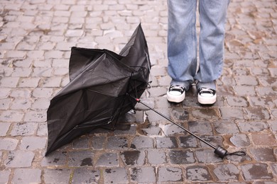 Photo of Woman and broken umbrella on wet pavement outdoors, closeup