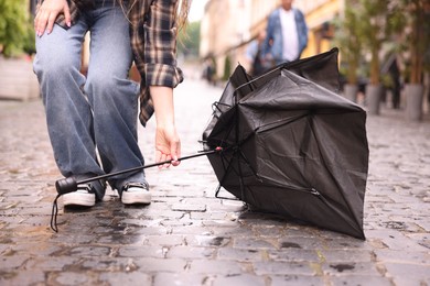 Photo of Woman taking broken umbrella on wet pavement outdoors, closeup