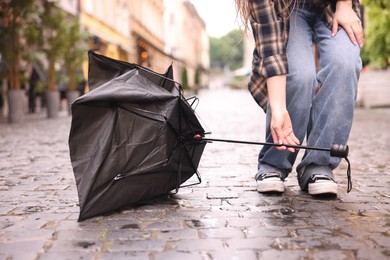 Photo of Woman taking broken umbrella on wet pavement outdoors, closeup