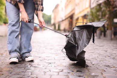 Photo of Woman with broken umbrella on wet pavement outdoors, closeup