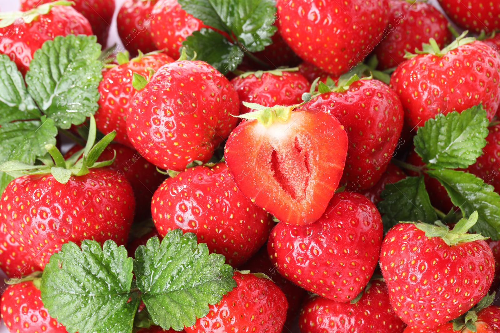 Fresh whole, cut strawberries and green leaves as background, top view Photo of Fresh whole, cut strawberries and green leaves as background, top view