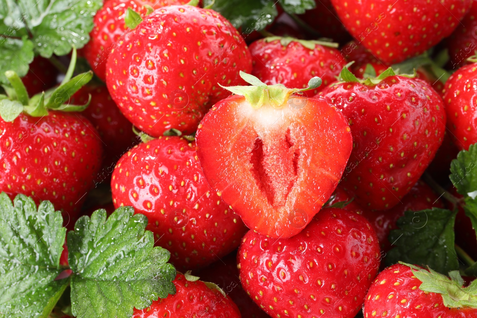 Photo of Fresh whole, cut strawberries and green leaves as background, closeup
