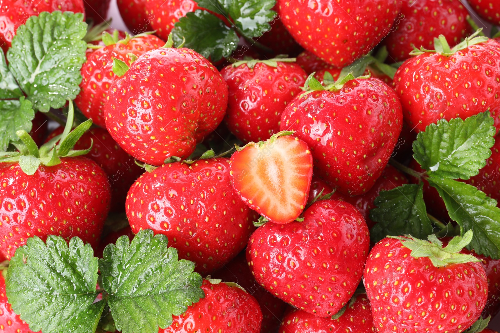 Fresh whole, cut strawberries and green leaves as background, top view Photo of Fresh whole, cut strawberries and green leaves as background, top view