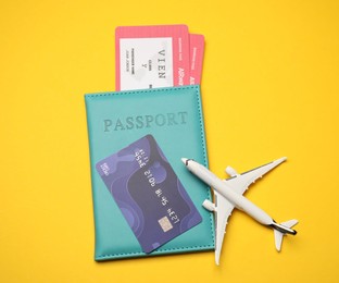 Photo of Passport with tickets, credit card and airplane model on yellow background, top view