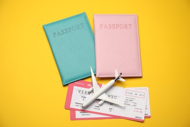 Photo of Passports with tickets and airplane model on yellow background, flat lay