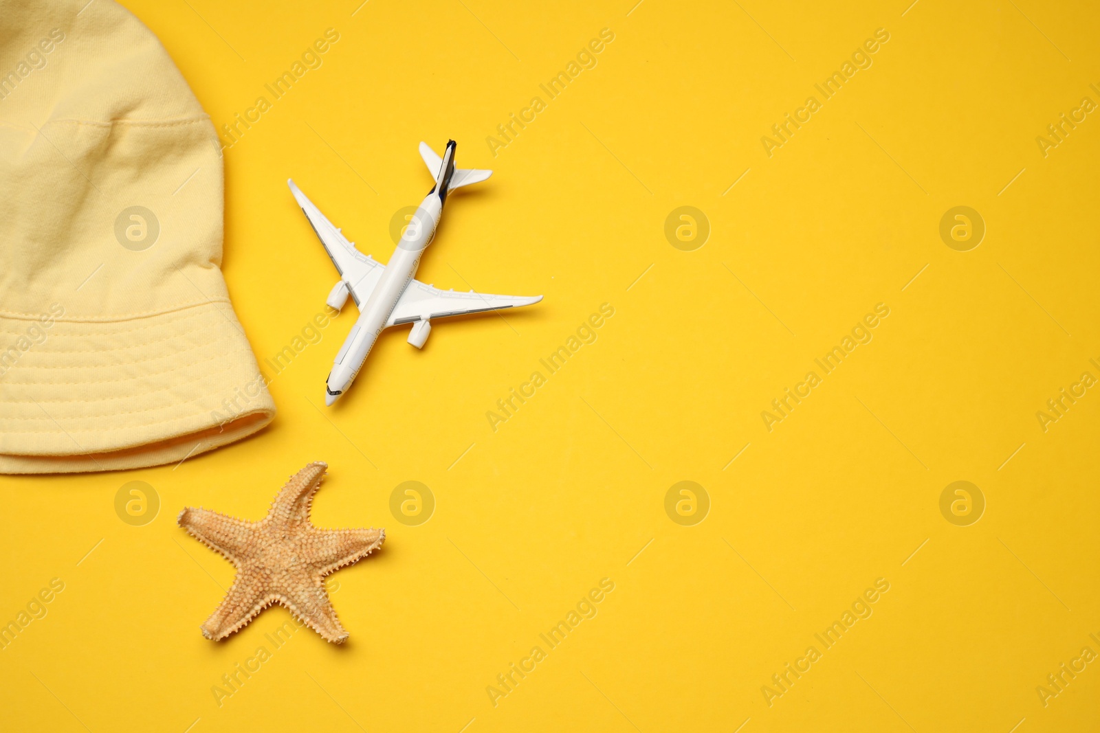 Airplane model, hat and starfish on yellow background, flat lay. Space for text Photo of Airplane model, hat and starfish on yellow background, flat lay. Space for text