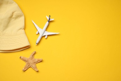 Photo of Airplane model, hat and starfish on yellow background, flat lay. Space for text