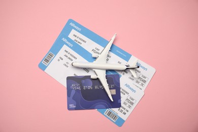 Photo of Airplane model, tickets and credit card on pink background, top view