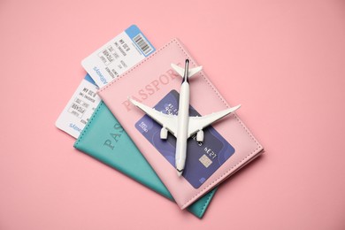 Photo of Passports with tickets, credit card and airplane model on pink background, top view