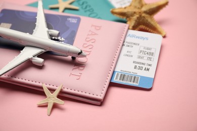 Photo of Passports with tickets, credit card, airplane model and starfishes on pink background, closeup