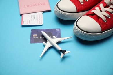 Photo of Passport with ticket, credit card, airplane model and shoes on light blue background, closeup