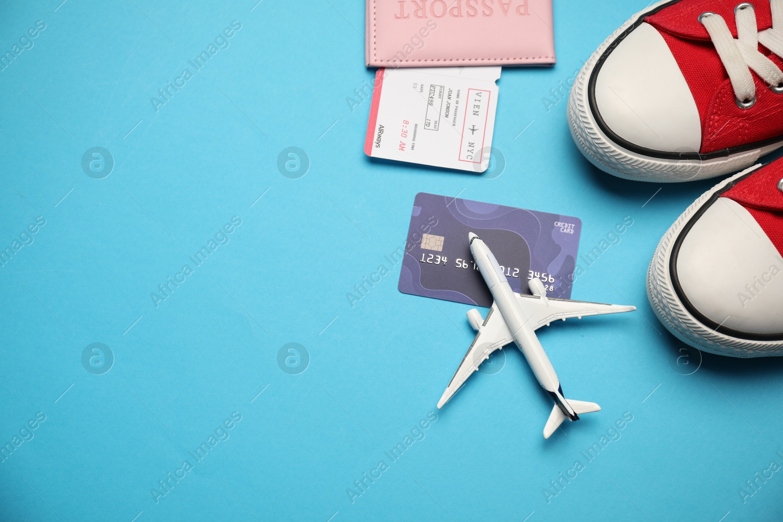 Passport with ticket, credit card, airplane model and shoes on light blue background, flat lay. Space for text Photo of Passport with ticket, credit card, airplane model and shoes on light blue background, flat lay. Space for text