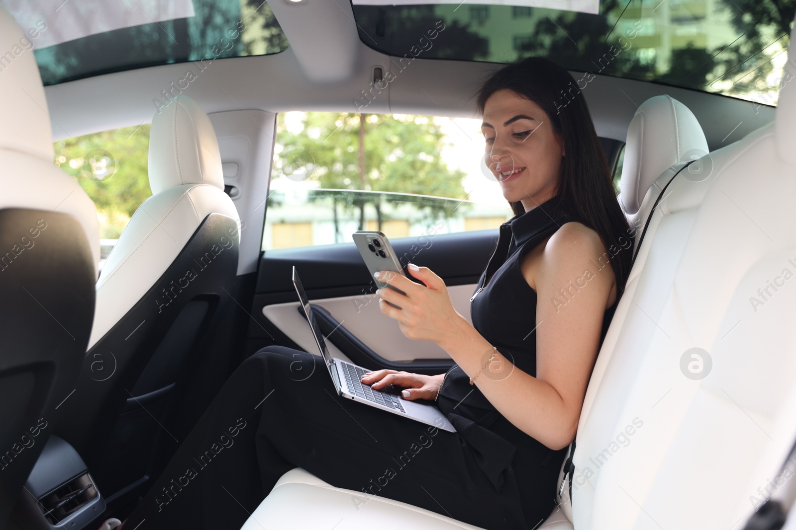 Woman with smartphone and laptop in modern car Photo of Woman with smartphone and laptop in modern car