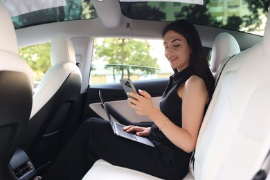 Photo of Woman with smartphone and laptop in modern car