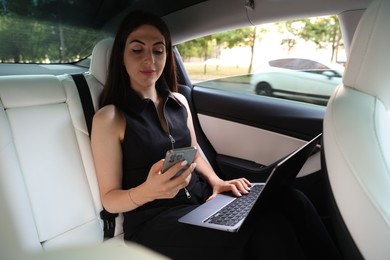 Photo of Woman with smartphone and laptop in modern car