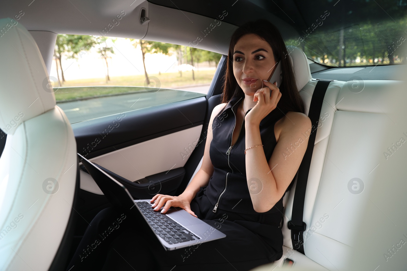 Woman with laptop talking on smartphone in modern car Photo of Woman with laptop talking on smartphone in modern car