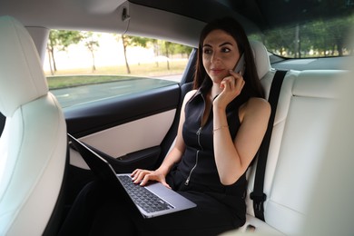Photo of Woman with laptop talking on smartphone in modern car