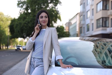 Photo of Beautiful woman talking on smartphone near car outdoors