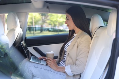 Photo of Woman with coffee and laptop in modern car, view from outside