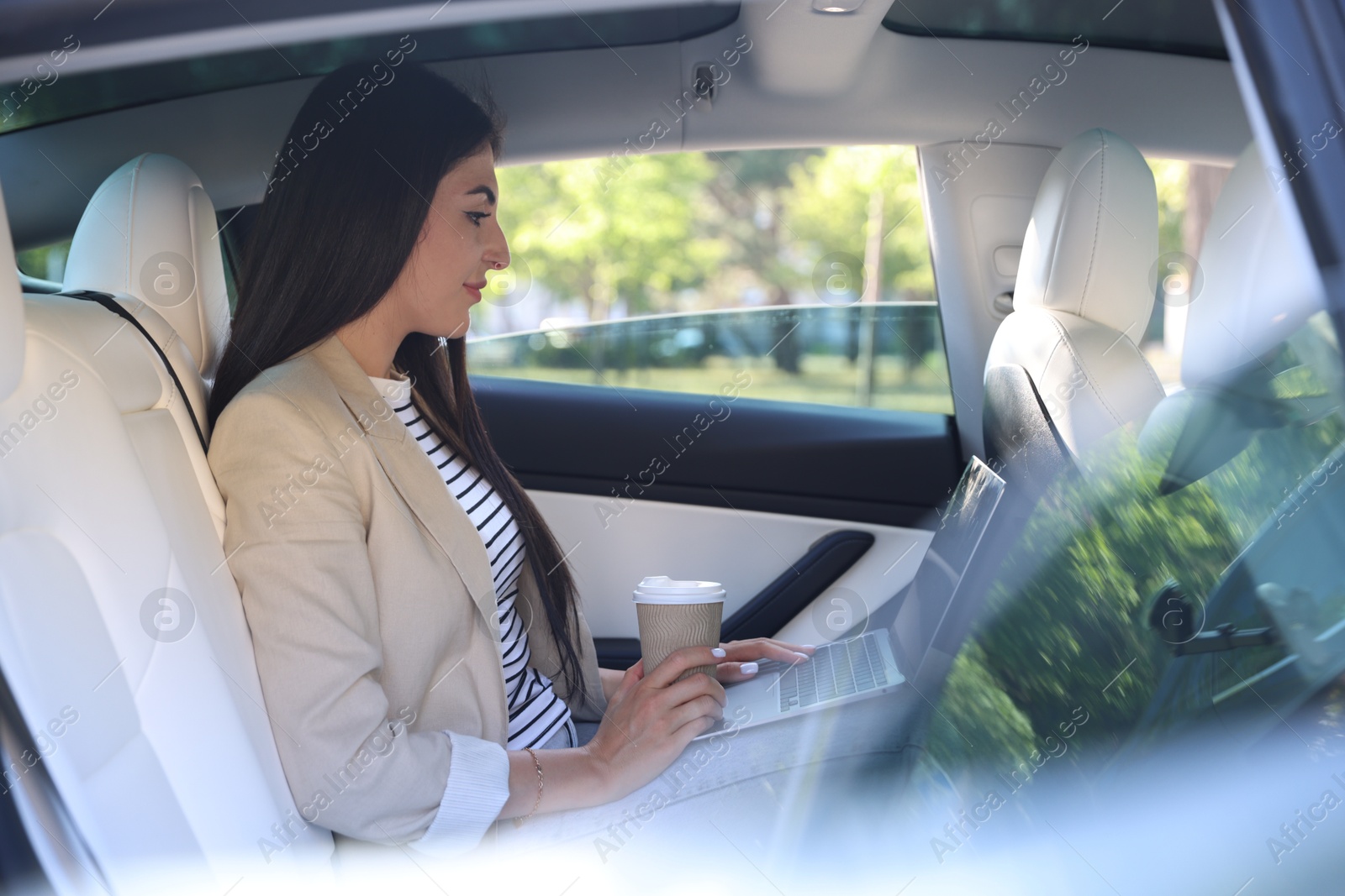 Woman with coffee and laptop in modern car, view from outside Photo of Woman with coffee and laptop in modern car, view from outside