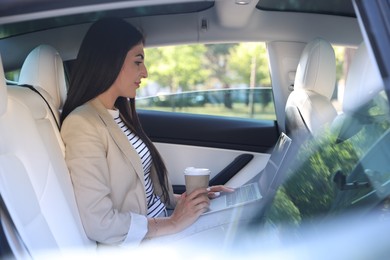 Photo of Woman with coffee and laptop in modern car, view from outside