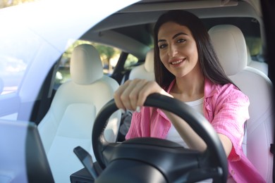 Photo of Woman behind steering wheel of modern car, view through windshield