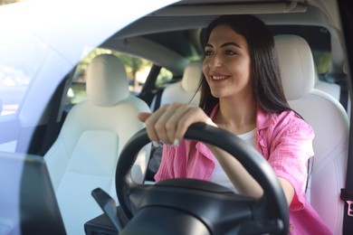 Photo of Woman behind steering wheel of modern car, view through windshield
