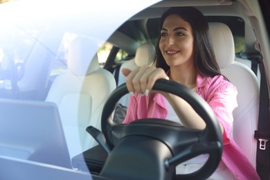 Photo of Woman behind steering wheel of modern car, view through windshield