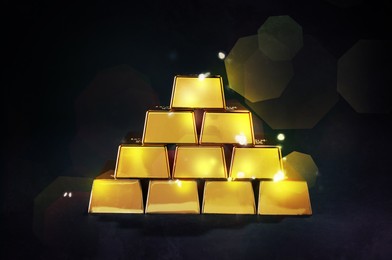 Image of Stacked shiny gold bars on black background. Space for text