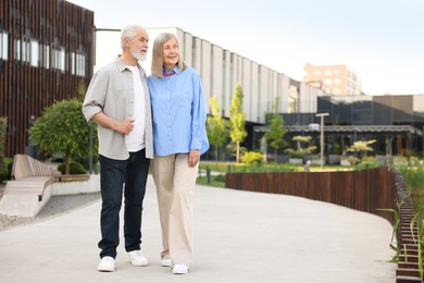Photo of Lovely senior couple walking together on city street, space for text