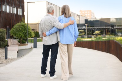 Photo of Lovely senior couple walking together on city street, back view