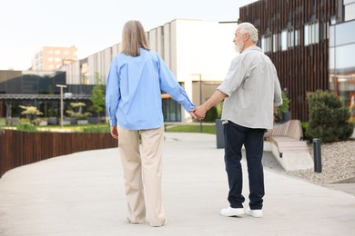 Photo of Lovely senior couple walking together on city street, back view