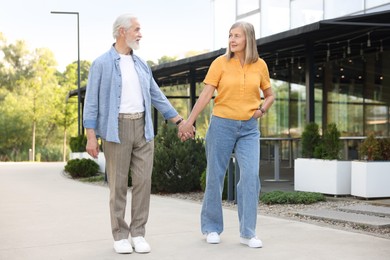 Photo of Lovely senior couple walking together near building outdoors
