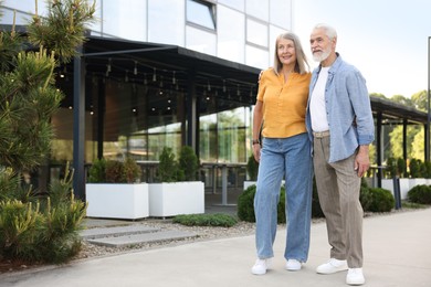 Photo of Lovely senior couple walking together near building outdoors, space for text