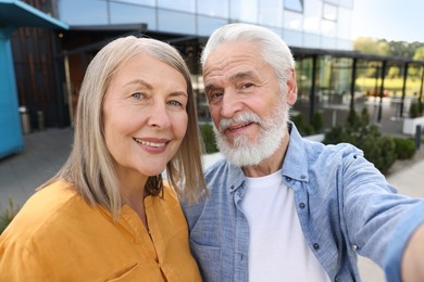 Photo of Lovely senior couple taking selfie near building outdoors