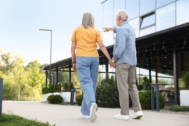 Photo of Lovely senior couple walking together near building outdoors, back view