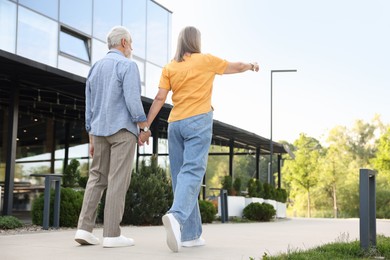 Photo of Lovely senior couple walking together near building outdoors, back view