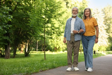 Photo of Lovely senior couple walking together in park, space for text