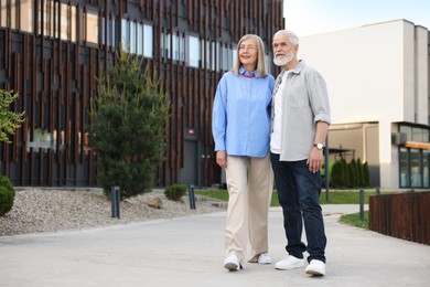 Photo of Lovely senior couple walking together in park, space for text