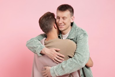 Photo of Two happy friends hugging on pink background